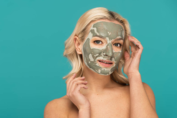 blonde woman with clay mask on face looking at camera isolated on turquoise - Photo, Image