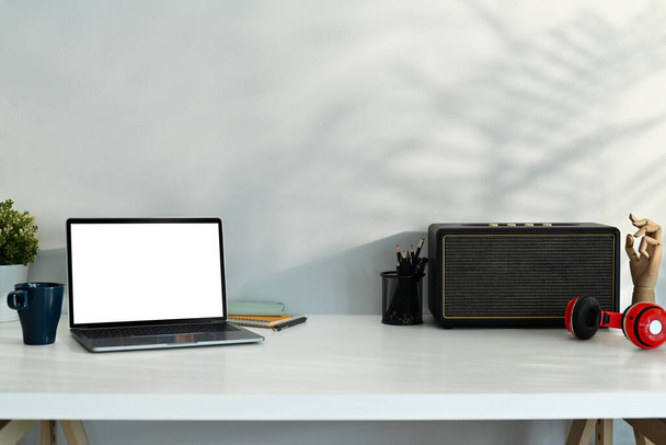 Stilvoller Arbeitsplatz mit Laptop, drahtlosem Lautsprecher und Kopfhörer auf weißem Tisch. - Foto, Bild