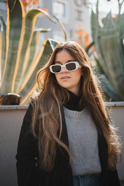 Portrait of a teenage girl wearing white sunglasses during a sunny day. There are plants at the background. - Foto, Imagem