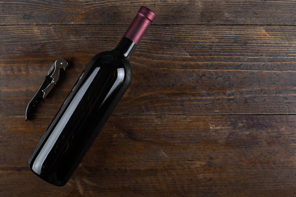 Corkscrew and a bottle of red wine on a wooden background. Top view with copy space - Фото, изображение