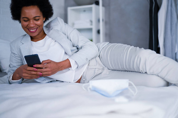 Giovane donna d'affari nera appena arrivata in hotel prendendo un periodo di riposo da un viaggio, utilizzando uno smartphone - Foto, immagini
