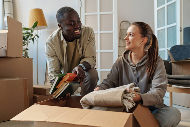Молодая счастливая пара распаковывает вещи вместе во время их переезда в новую квартиру - Фото, изображение