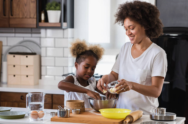 Madre enseñando a su hijo a cocinar y ayudar en la cocina. Madre e hija afroamericana haciendo galletas en casa. - Foto, imagen