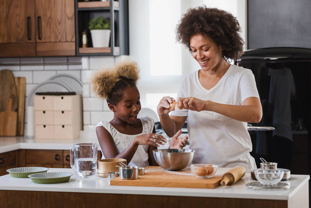 母は台所で調理し、助けるために子供を教える。アフリカ系アメリカ人の母親と娘は家でクッキーを作る. - 写真・画像