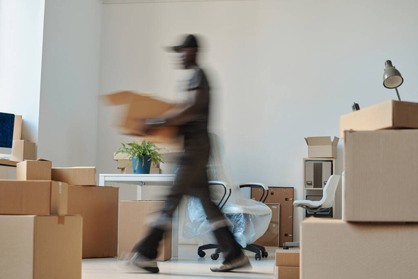 新しいオフィスに移転中に箱を運ぶアフリカ系アメリカ人労働者のぼやけた動き - 写真・画像
