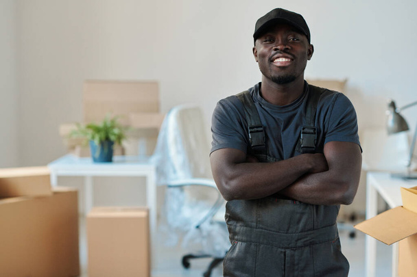Retrato del cargador afroamericano de pie con los brazos cruzados en la oficina y sonriendo a la cámara - Foto, Imagen
