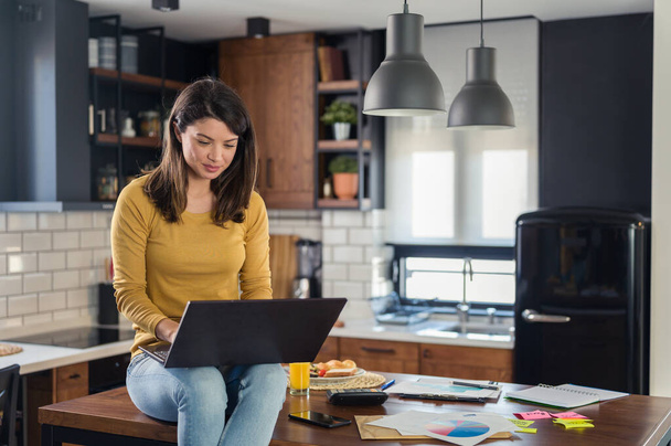 Młoda uśmiechnięta bizneswoman pracująca w domu, siedząca przed laptopem w kuchni domowej - Zdjęcie, obraz