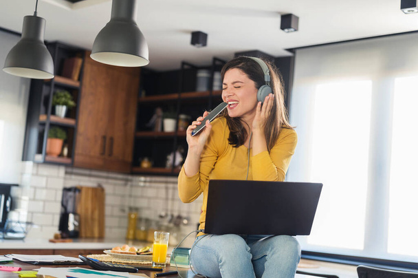 Young smiling woman with headphones working from home, taking break listening music and singing. Positive emotions. Woman with positive attitude. - Foto, Bild