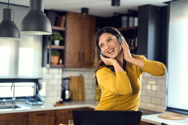 Young smiling woman with headphones working from home, taking break listening music and singing. Positive emotions. Woman with positive attitude. - Foto, afbeelding