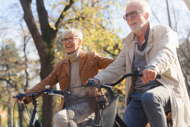 Alegre pareja mayor activa con bicicletas en el parque público juntos divertirse. Actividades perfectas para personas mayores. Feliz pareja adulta montando bicicletas en el parque - Foto, imagen