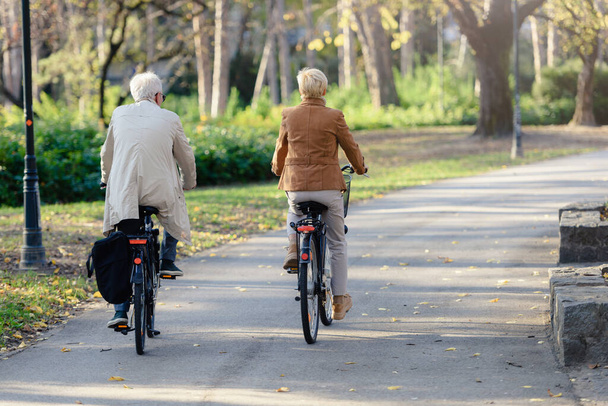 Весела активна старша пара з велосипедами в громадському парку разом розважається. Ідеальні заняття для літніх людей. Щаслива зріла пара їде на велосипедах в парку
 - Фото, зображення