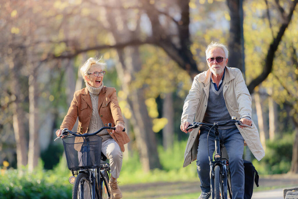 Fröhlich aktives Seniorenpaar mit Fahrrädern im öffentlichen Park beim gemeinsamen Spaß. Perfekte Aktivitäten für ältere Menschen. Glückliches älteres Paar fährt Fahrrad im Park - Foto, Bild