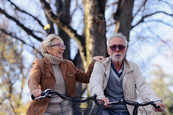 公共公園で自転車と陽気なアクティブなシニアカップルが一緒に楽しみを持っています。高齢者のための完璧な活動。公園で幸せな成熟したカップル乗馬自転車 - 写真・画像