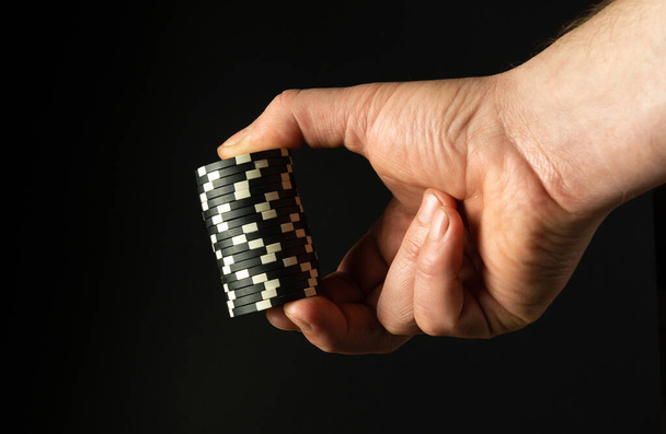 Primo piano della mano di un giocatore con chip di poker mentre scommette per vincere. Spazio libero per la pubblicità su sfondo nero. - Foto, immagini