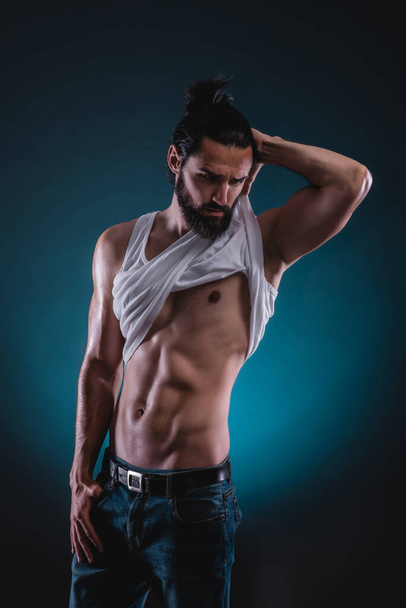 Studio portrait of a beautiful masculine bearded shirtless man showing his abdomen muscles - Photo, image