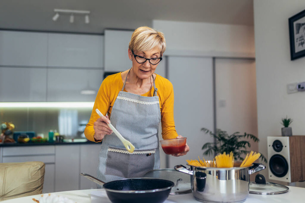Modern mutfağında yemek pişiren son sınıf mutlu bir kadın. - Fotoğraf, Görsel