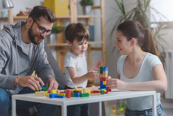 幸せな家族だ。教育的な木製のおもちゃを使用して自宅で彼女のかわいい幼児の息子と遊ぶ母親と父親。家庭教育 - 写真・画像