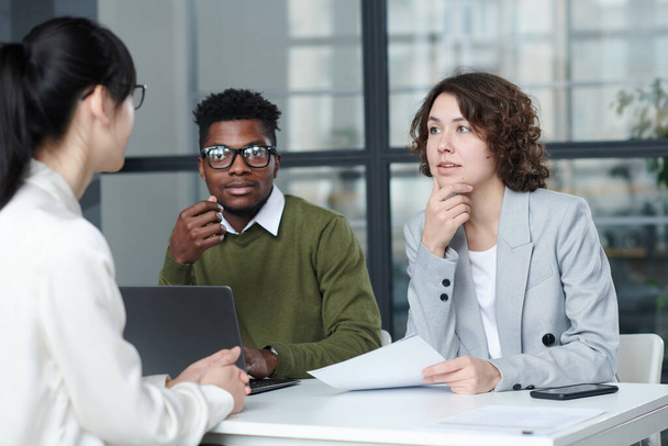 Business people asking questions to candidate while sitting at table during job interview - Photo, image