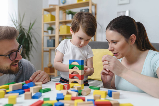 Genç ve mutlu bir aile. Anne ve baba, küçük tatlı oğluyla evde didactik tahta oyuncaklar kullanarak oynuyorlar. Evde eğitim - Fotoğraf, Görsel