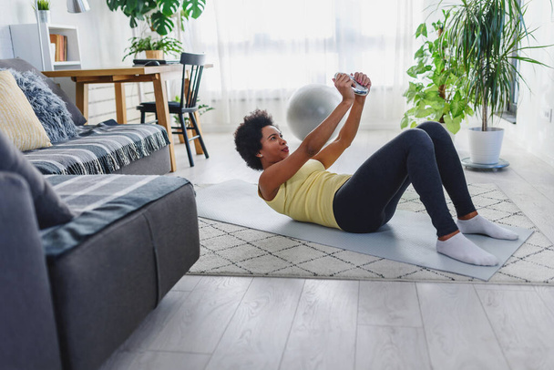 Afro-Amerikaanse vrouw doet oefeningen op de vloer in haar huis. Proberen gezond en fit te blijven. - Foto, afbeelding