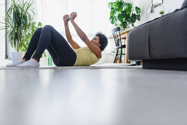 Afroamerikanerin bei Übungen auf dem Boden in ihrem Haus. Der Versuch, gesund und fit zu bleiben. - Foto, Bild