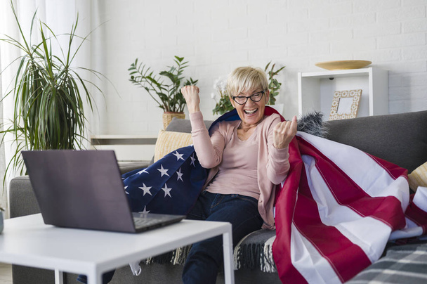 Vecchia signora americana a guardare le partite, tifo con una bandiera americana a sostegno della sua squadra. - Foto, immagini