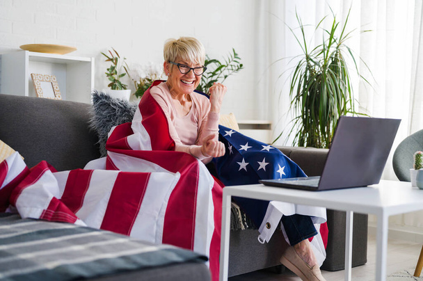 アメリカ人の老婦人は試合を見てチームを支えるアメリカ国旗で応援しています. - 写真・画像