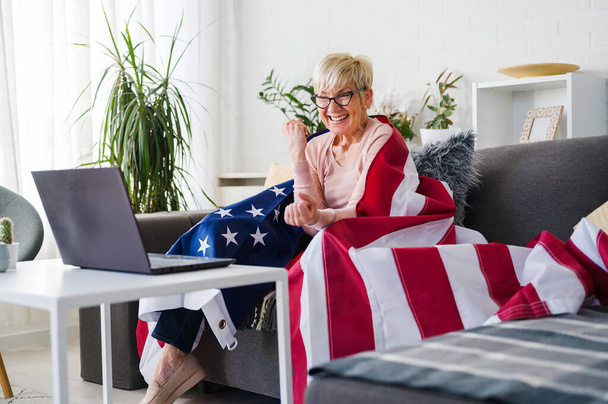 Vieja dama americana viendo partidos, vitoreando con una bandera americana apoyando a su equipo. - Foto, imagen