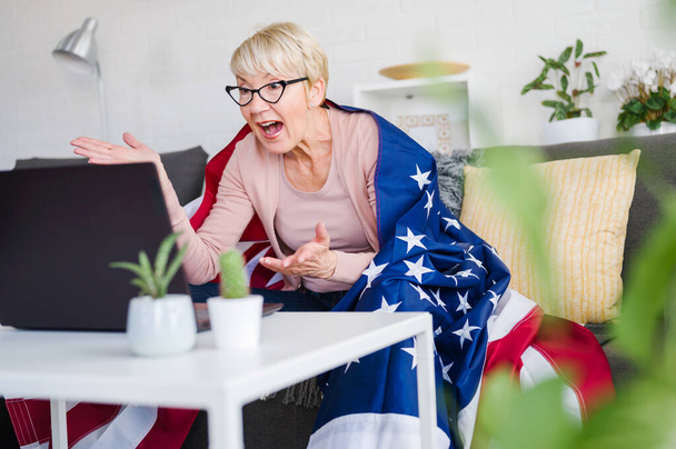 Velha senhora americana assistindo jogos, torcendo com uma bandeira americana apoiando sua equipe. - Foto, Imagem