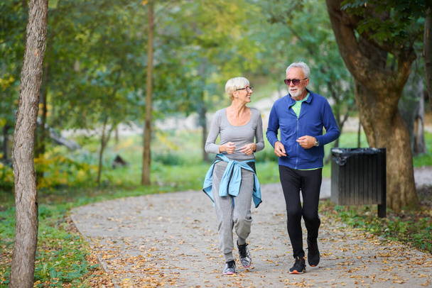 Cheerful, active senior couple jogging in the park. Exercise together to stop aging. - Photo, Image
