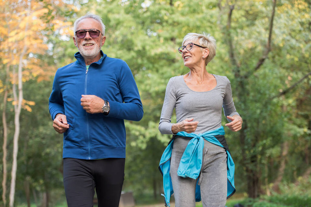 Cheerful, active senior couple jogging in the park. Exercise together to stop aging. - Foto, afbeelding