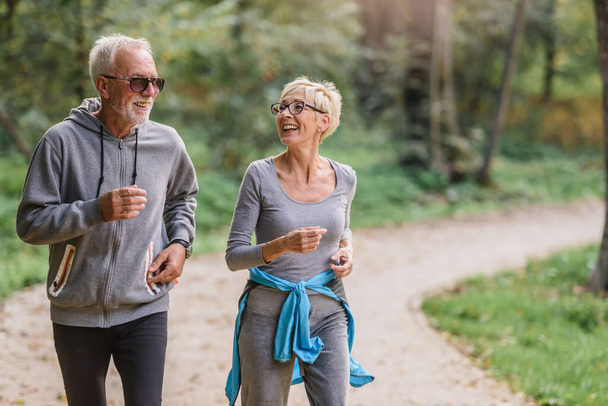 Cheerful, active senior couple jogging in the park. Exercise together to stop aging. - Fotoğraf, Görsel