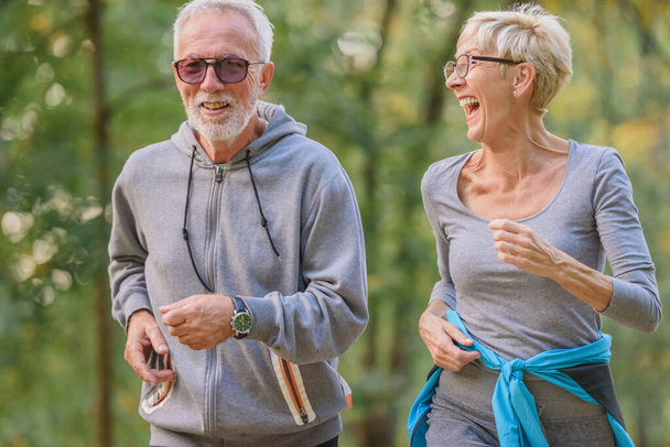 Веселая, активная старшая пара бегает в парке. Упражнения вместе, чтобы остановить старение. - Фото, изображение