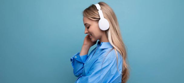une fille dans les grands écouteurs sans fil bénéficie et se détend à la musique de l'application sur un fond bleu. - Photo, image