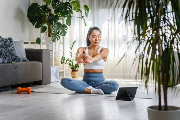 Молодая азиатка инструктор yoga использующ планшетный ПК на online классе yoga - Фото, изображение