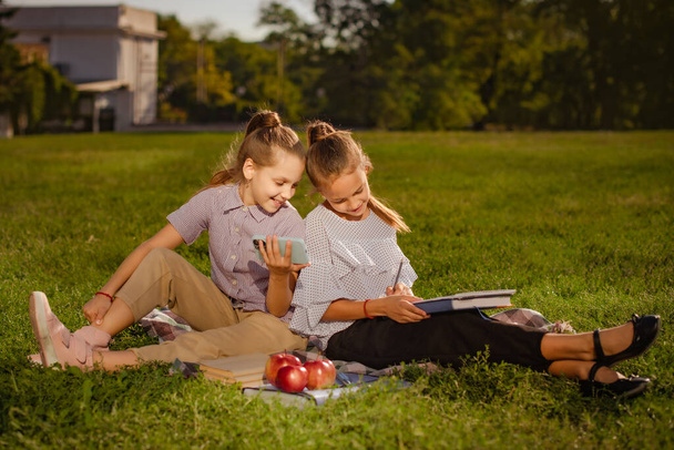 teen girls prepare together for passing tests and exams. girls drawing using an example in mobile application in nature sitting in park - Foto, Imagem