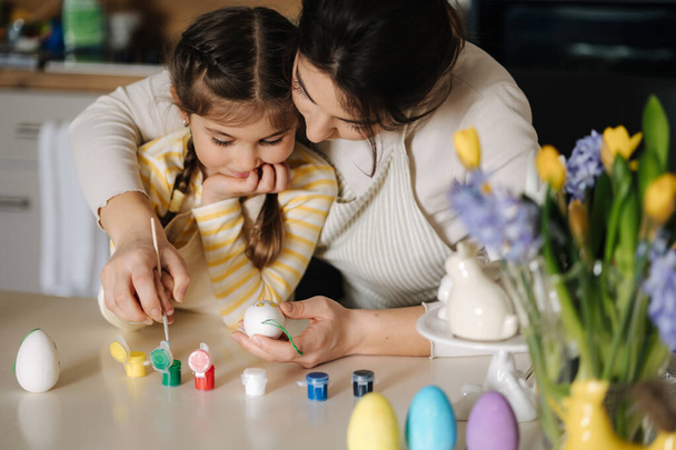 Portrait of mom and daughter painting easter eggs on kitchen. Spring holidays mood. Family. High quality photo - Photo, Image