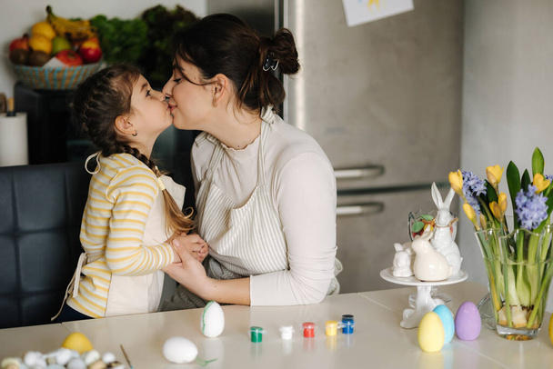 Cute little girl with her mother preparing for painting easter eggs. Mom and daughter in apron. High quality photo - Valokuva, kuva