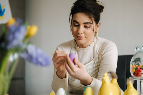 Ελκυστική νεαρή γυναίκα ζωγραφίζει πασχαλινά αυγά στην κουζίνα. Εαρινές διακοπές. . Υψηλής ποιότητας φωτογραφία - Φωτογραφία, εικόνα