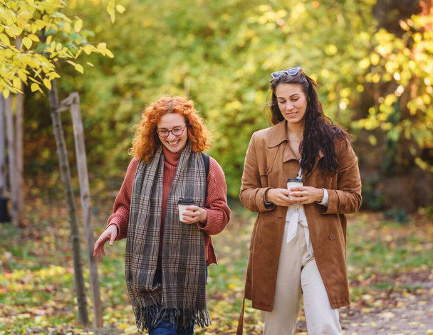 Két gyönyörű nő sétál a szabadban kávéval. - Fotó, kép