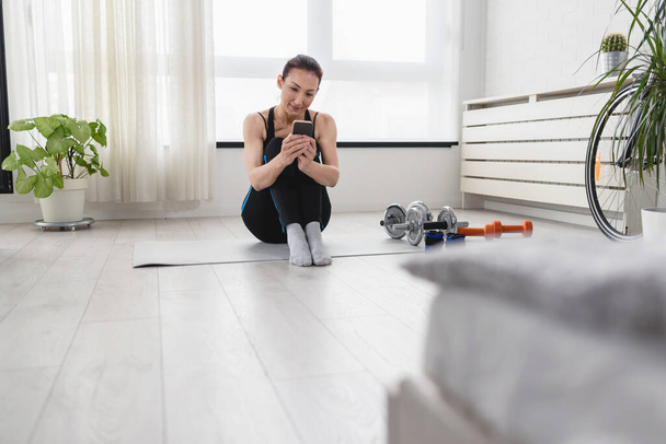 Woman using smartphone during exercise in the morning at home - Photo, image