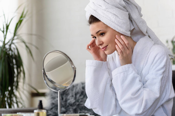 belle jeune femme en peignoir et serviette regardant miroir, concept de soins de la peau - Photo, image