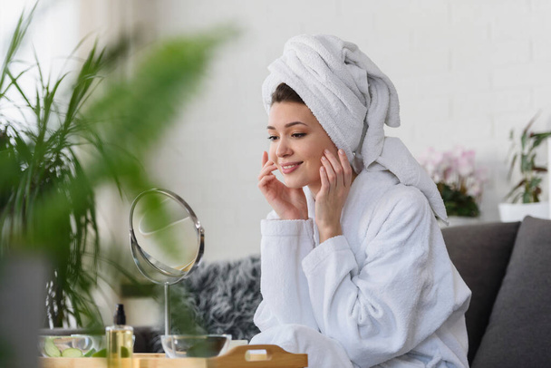 beautiful young woman in bathrobe and towel looking at mirror, skincare concept - Foto, imagen