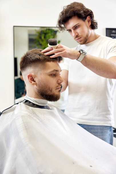 Barber trim hair with clipper on handsome bearded man in barber shop. - Foto, Bild