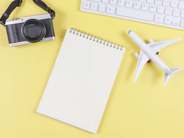 Top view or flat lay of airplane model, computer keyboard, opened blank page notebook and digital camera with copy space on yellow background, business and traveling concept. - Foto, afbeelding