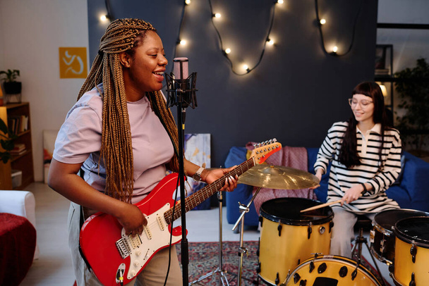 Афроамериканка поет песни в микрофоне и репетирует со своим другом, играющим на барабанах в студии - Фото, изображение