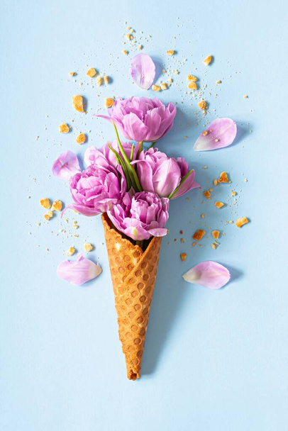 Wafer (waffle) cone with tulips on blue background. Flower ice cream, spring concept with first flowers, mother's day, top view. - Photo, Image