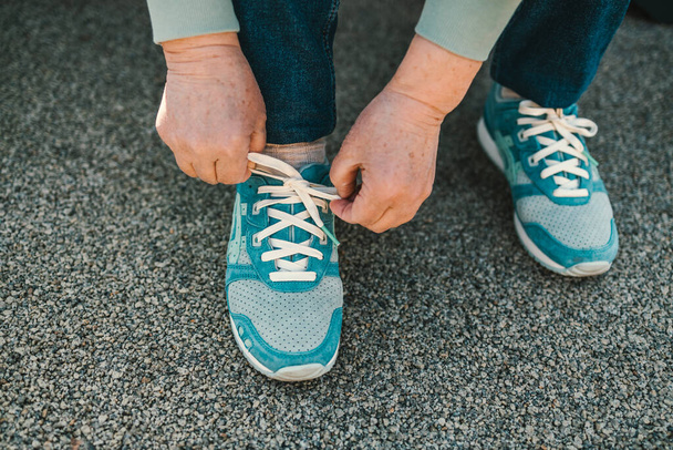 Close-up vintage beeld van de vrouw hand gezet op blauwe sneaker over betonnen vloer voor wandelen. . Hoge kwaliteit foto - Foto, afbeelding