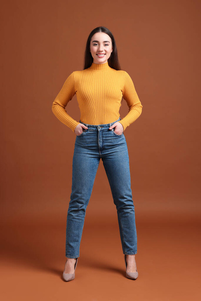 Young woman in stylish jeans on brown background - Fotoğraf, Görsel