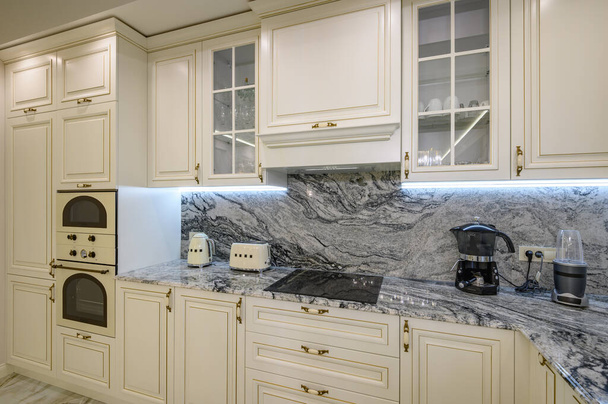 Close-up van de klassieke crèmekleurige keuken met apparaten aan de toonbank, waaronder oven, magnetron en koffiezetapparaat - Foto, afbeelding